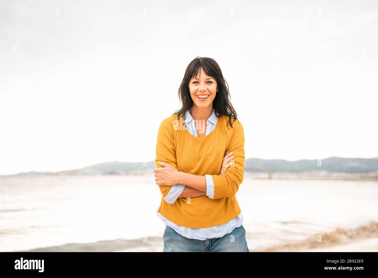 Glückliche Frau mit verschränkten Armen am Strand Stockfoto