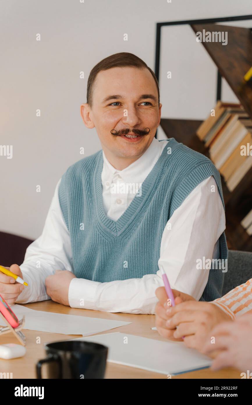 Geschäftsmann mit Schnurrbart, sitzt am Tisch und hört Kollegen zu Stockfoto