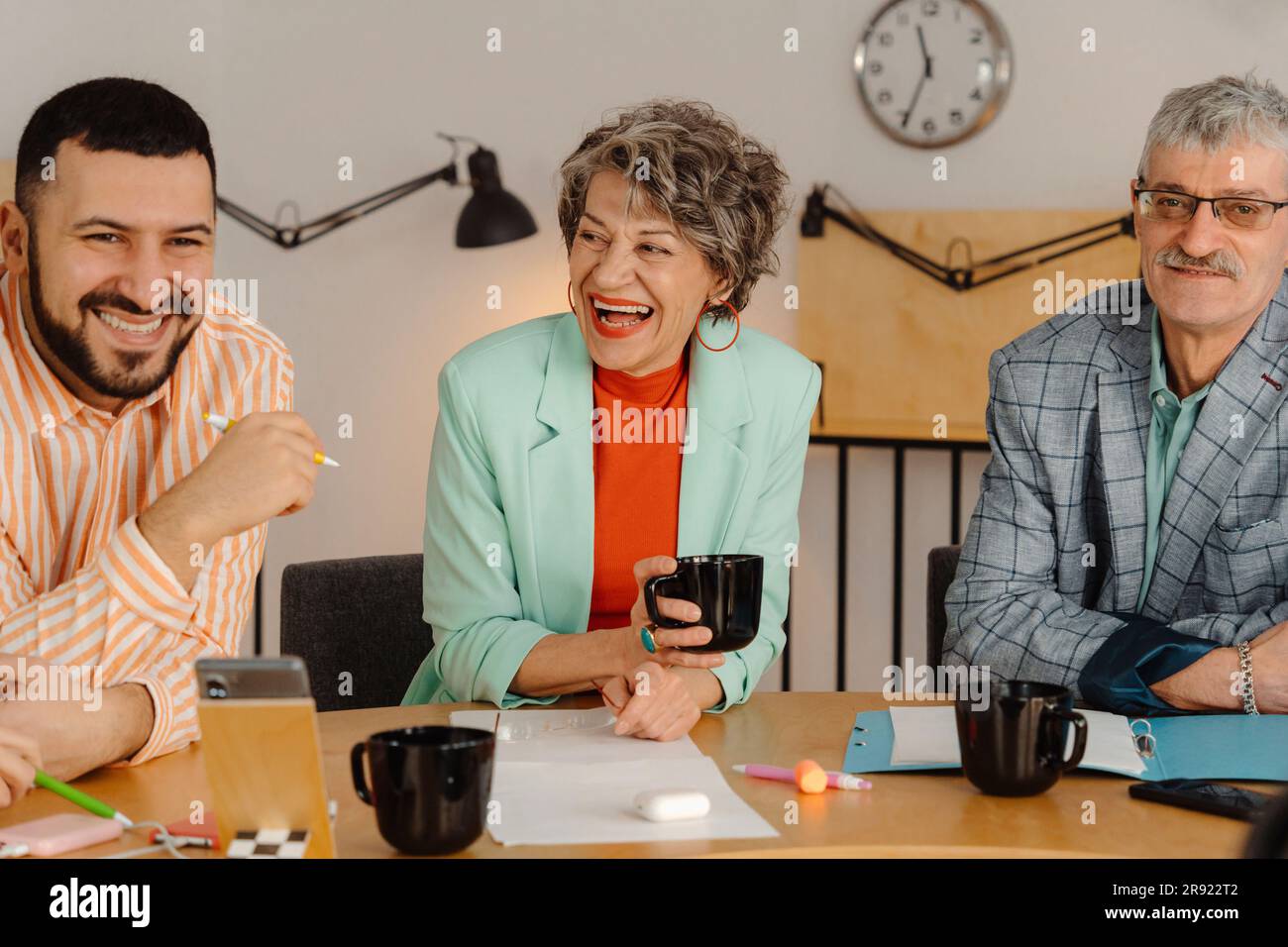 Kollegen, die am Tisch sitzen und lachen und miteinander reden Stockfoto
