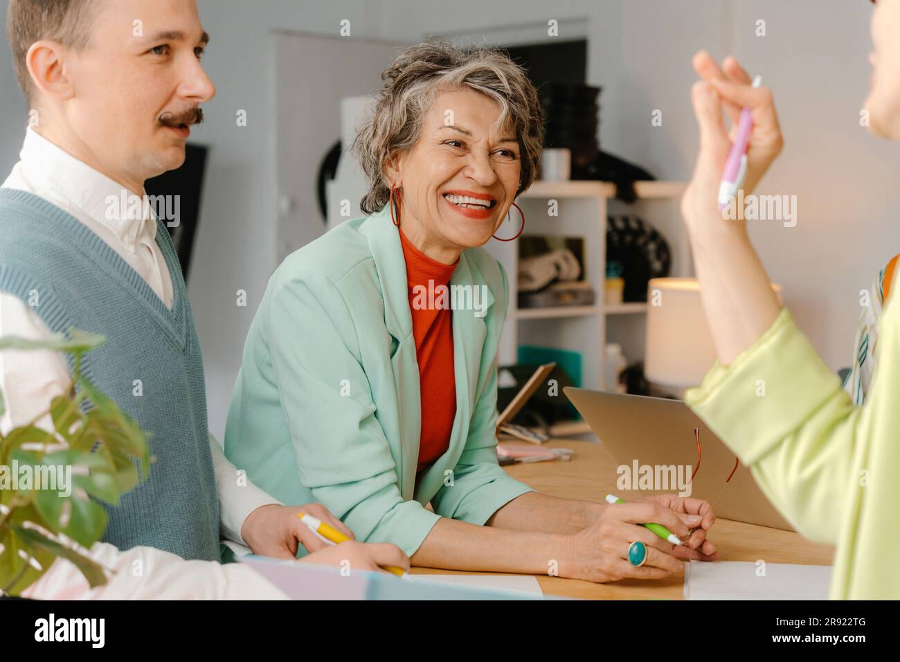 Eine Frau in leuchtenden Klamotten spricht mit Kollegen und amüsiert sich im Studio Stockfoto
