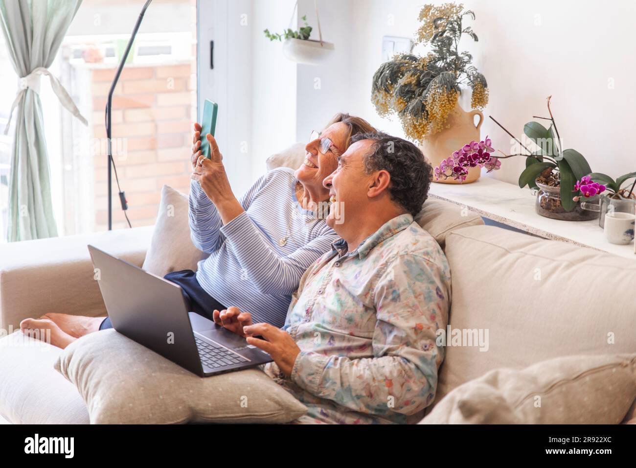 Glückliches Seniorenpaar, das zu Hause Freizeit mit Wireless-Technologien verbringt Stockfoto