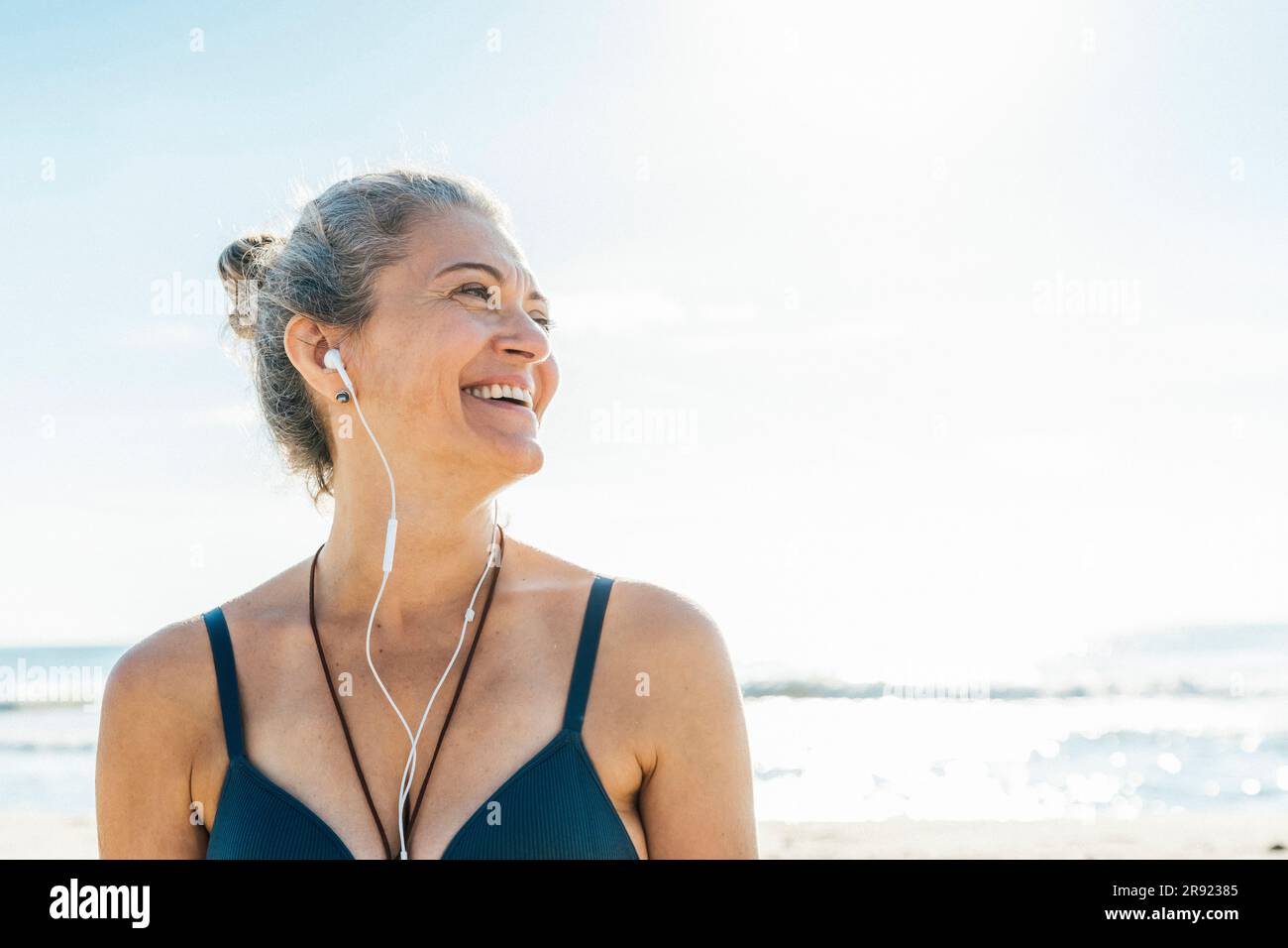 Glückliche Frau mit InEar-Kopfhörern, die sich am Strand umsieht Stockfoto