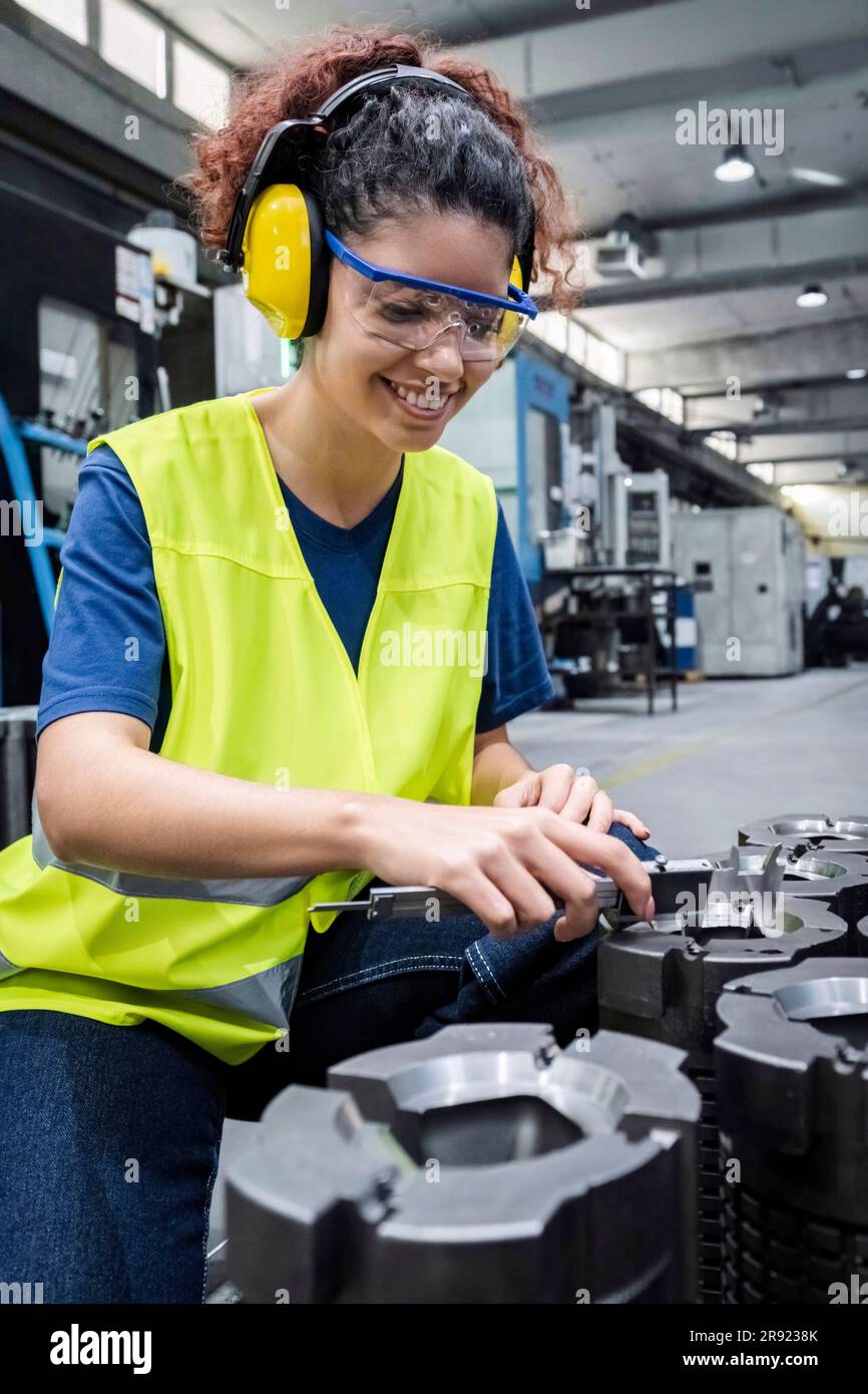 Lächelnder Ingenieur in reflektierender Kleidung, der in einer modernen Fabrik arbeitet Stockfoto