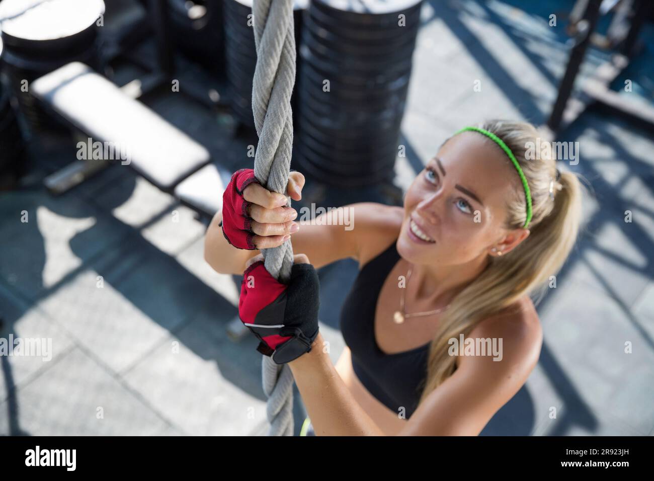 Lächelnde Frau, die im Fitnessstudio auf dem Dach ein Seil hochklettert Stockfoto