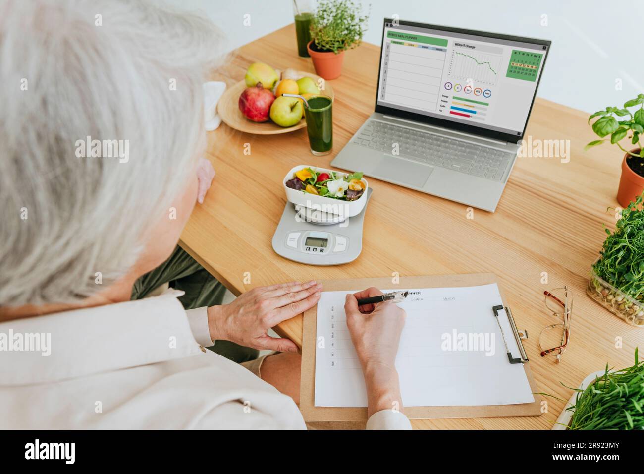 Ernährungswissenschaftler schreibt auf dem Klemmbrett mit Diätessen auf dem Tisch zu Hause Stockfoto