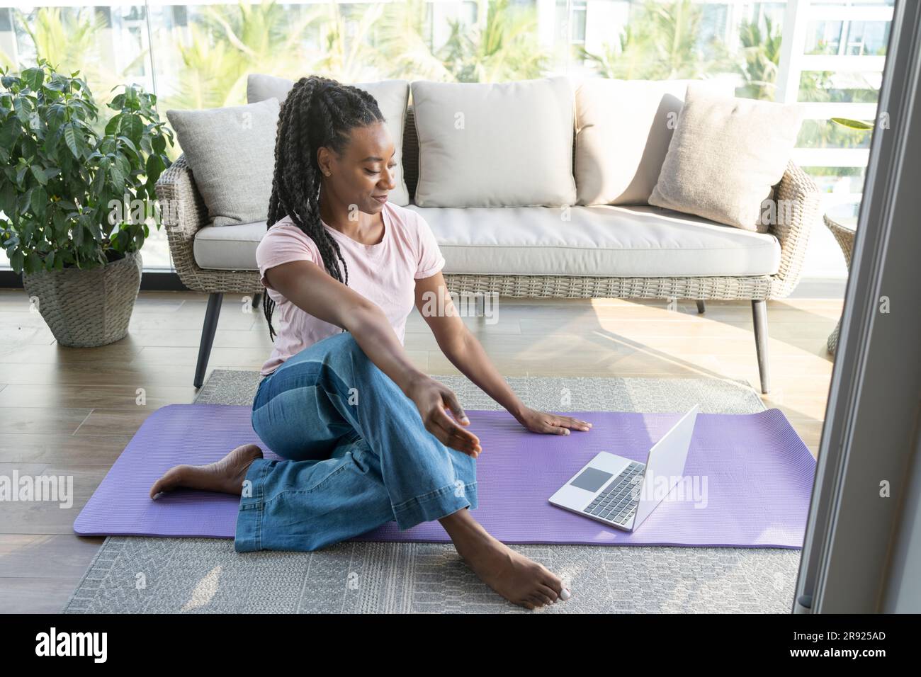 Lächelnde Frau, die zu Hause auf einer Yoga-Matte mit einem Laptop sitzt Stockfoto