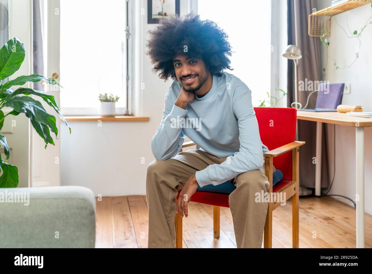 Lächelnder Mann, der zu Hause auf einem Stuhl sitzt Stockfoto