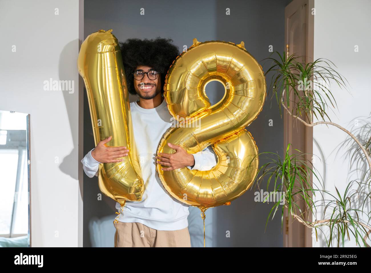 Ein lächelnder Mann, der zu Hause einen Ballon mit einer Nummer von 18 hält Stockfoto