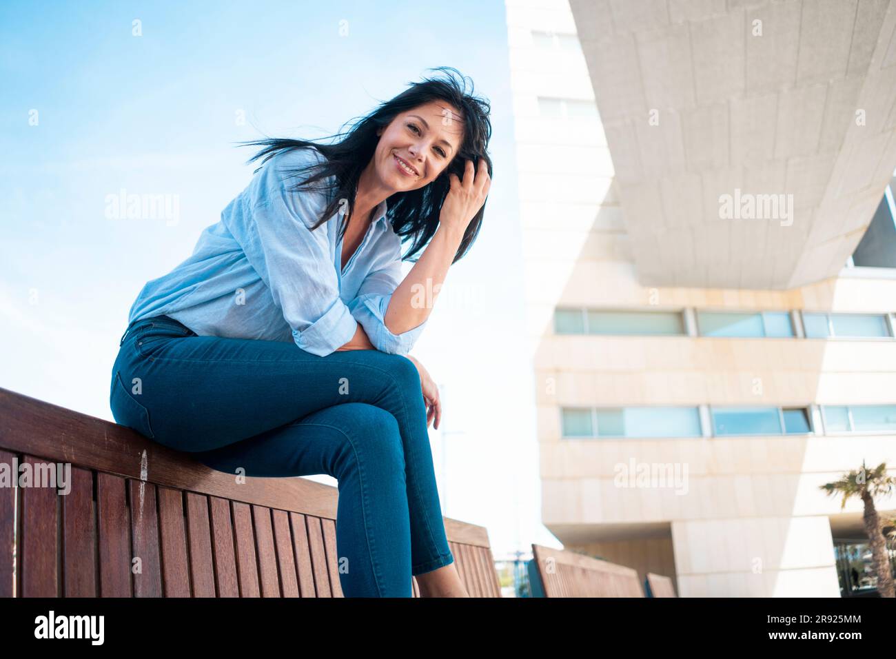 Lächelnde Geschäftsfrau mit Hand im Haar, die auf einer Bank sitzt Stockfoto