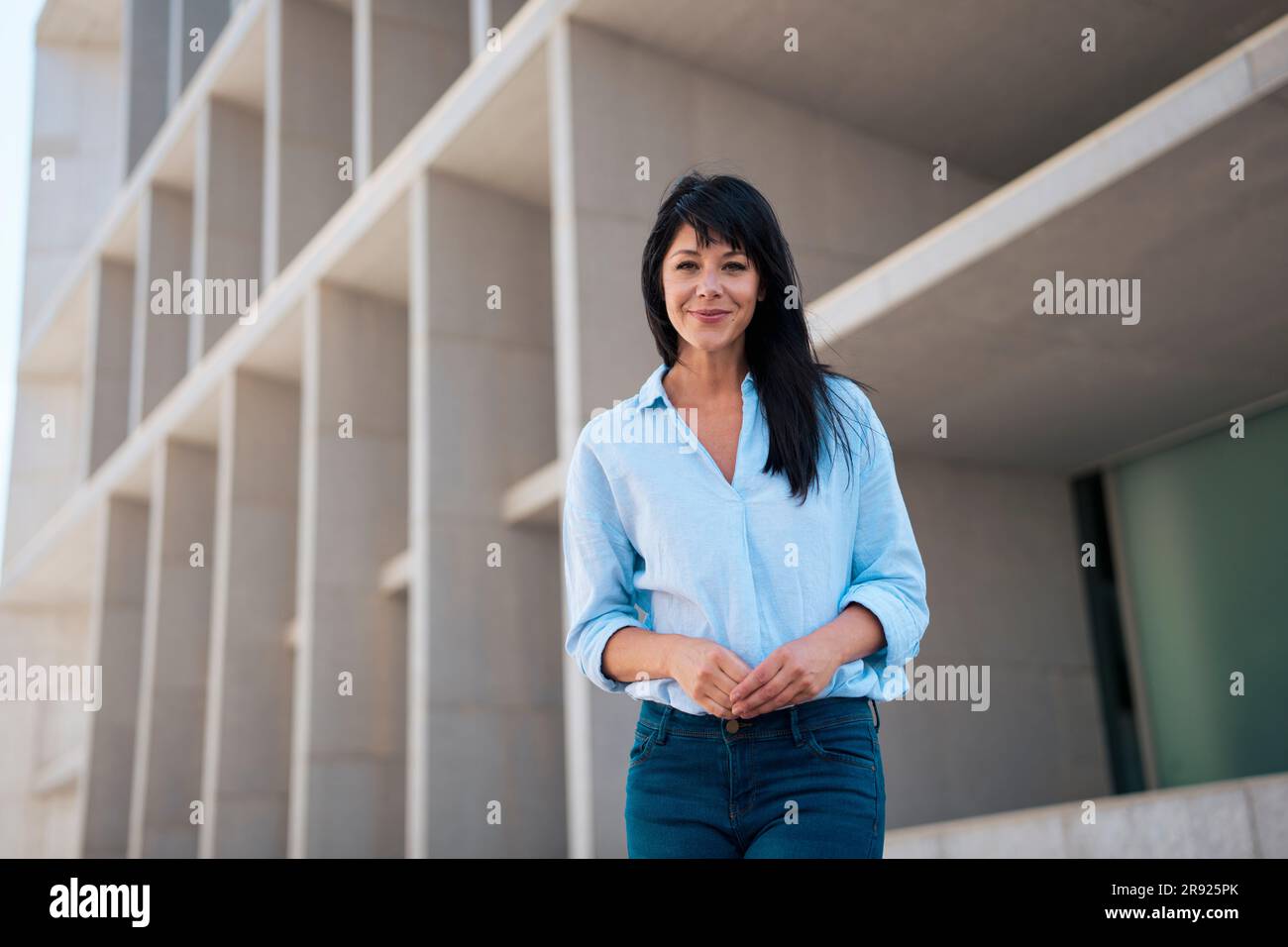Lächelnde, reife Geschäftsfrau, die ein blaues Hemd vor dem Gebäude trägt Stockfoto