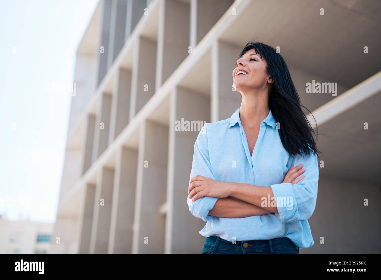 Lächelnde Geschäftsfrau in blauem Hemd, die mit gekreuzten Armen steht Stockfoto