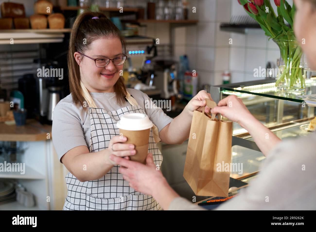 Lächelnder Cafebesitzer mit Down-Syndrom, der dem Gast Essen zum Mitnehmen gibt Stockfoto