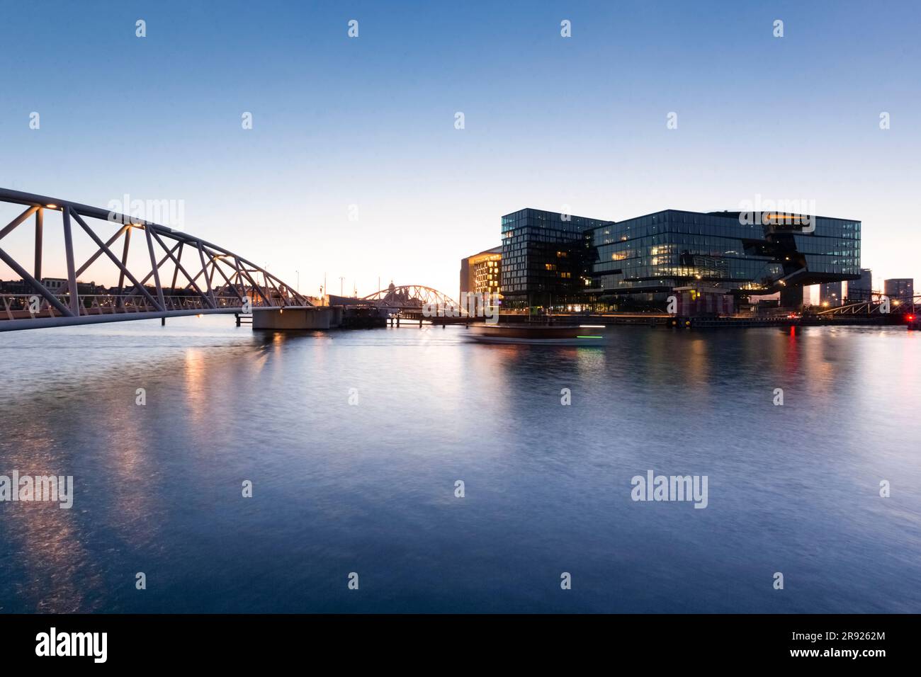 Niederlande, Nordholland, Amsterdam, Brücke über den städtischen Kanal in der Dämmerung mit modernen Gebäuden im Hintergrund Stockfoto