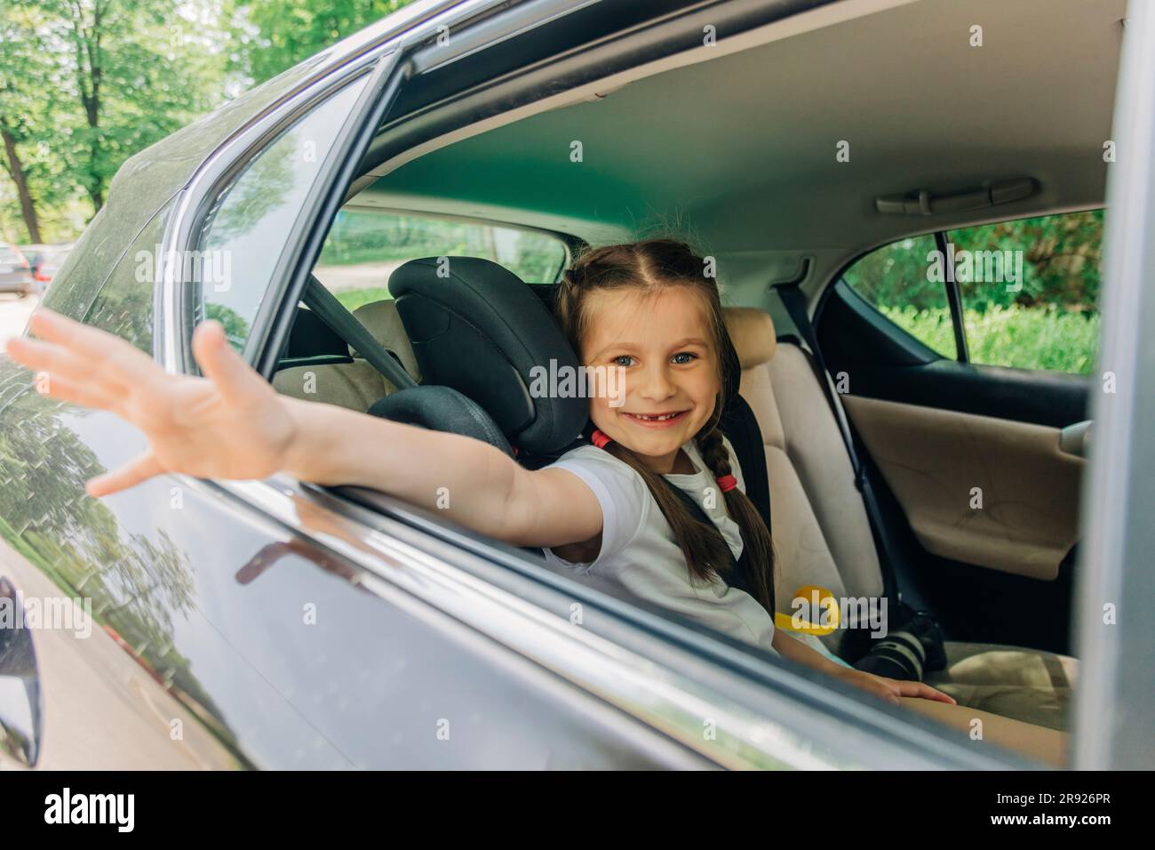 Glückliches Mädchen, das im Auto mit der Hand winkt Stockfoto
