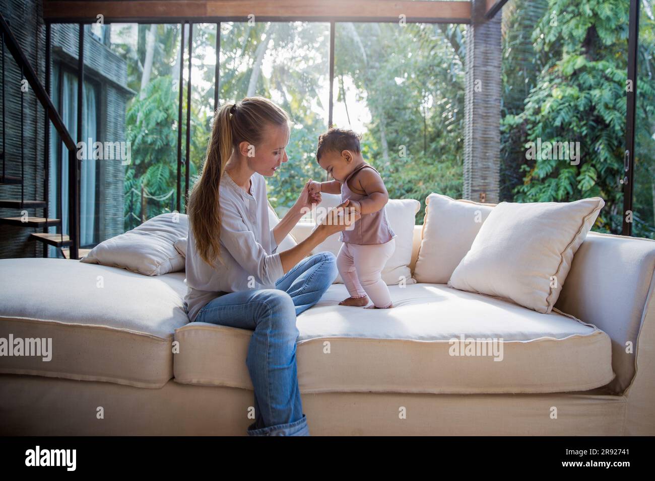 Mutter mit Baby-Tochter, die zu Hause auf dem Sofa steht Stockfoto