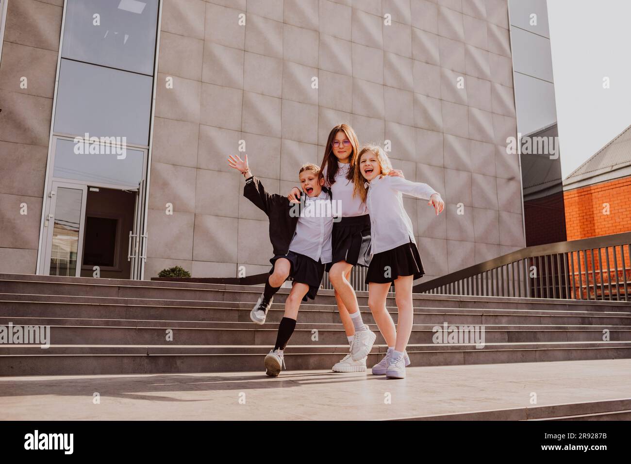 Glückliche Schulmädchen, die sich in der Nähe der Treppe vor dem Schulgebäude amüsieren Stockfoto