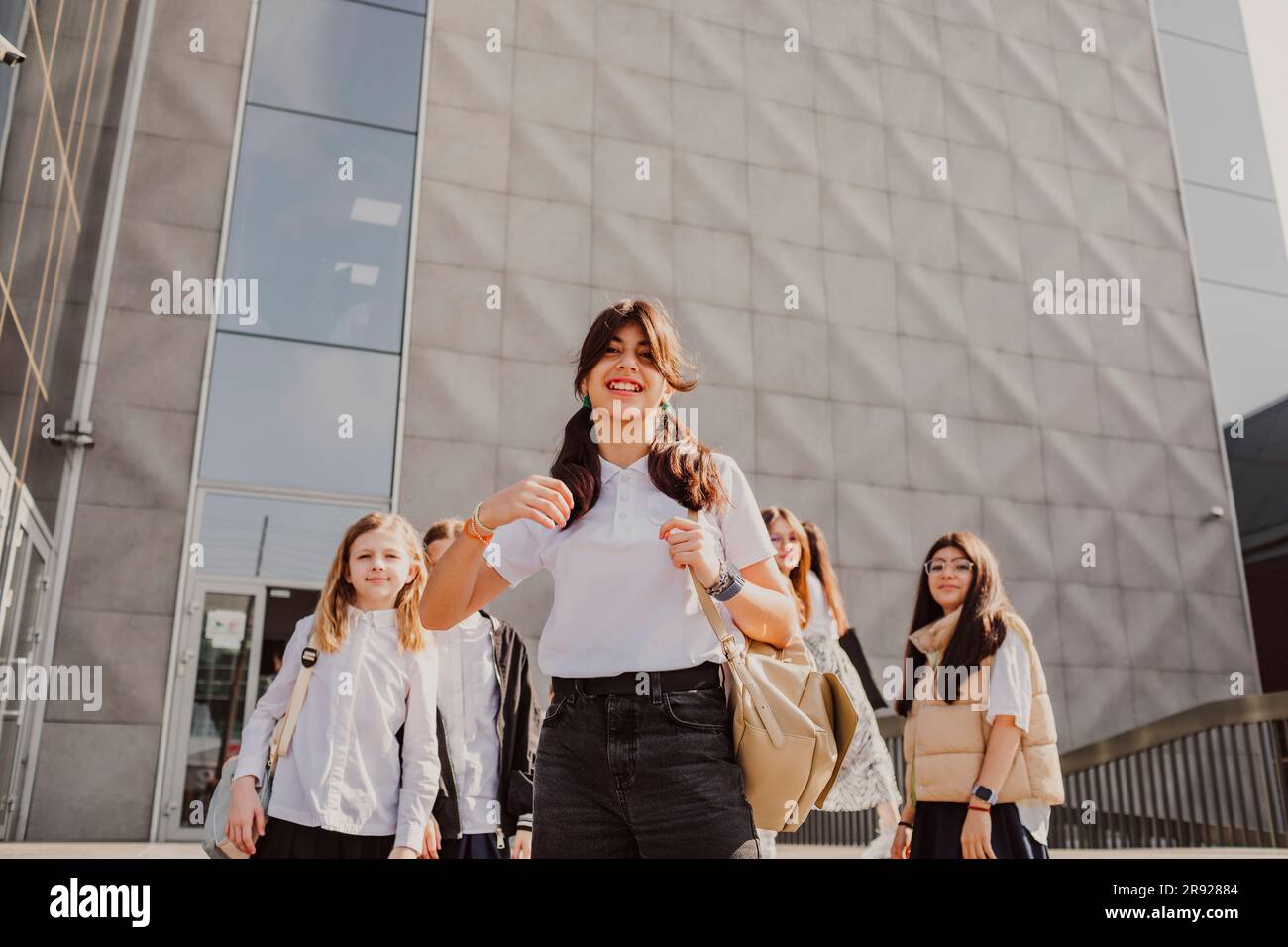 Lächelndes Mädchen mit Schulfreunden, die vor dem Gebäude stehen Stockfoto