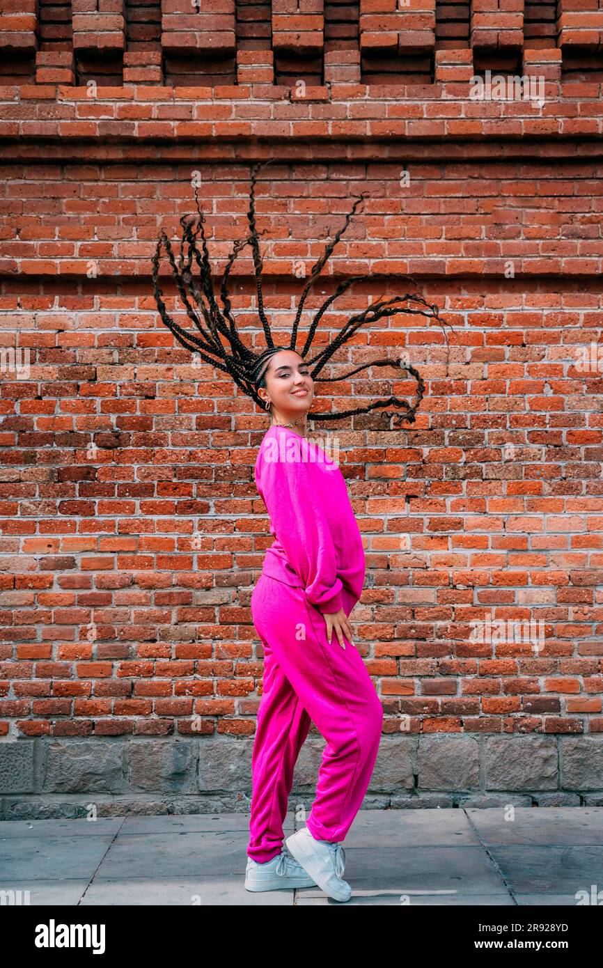 Lächelnde Frau mit Dreadlocks, die vor einer Ziegelwand steht Stockfoto