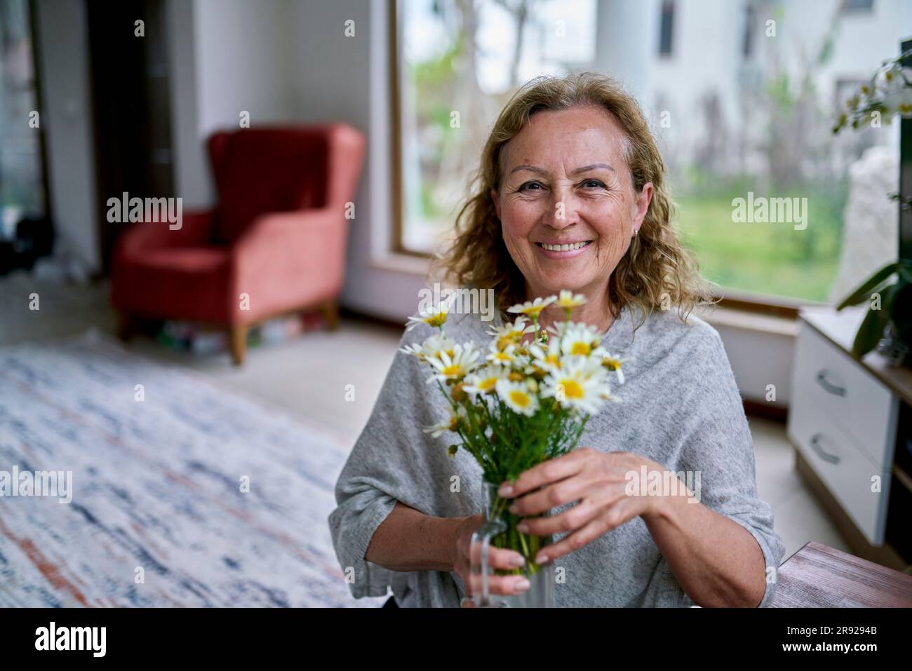 Glückliche Seniorin mit Blumenvase zu Hause Stockfoto