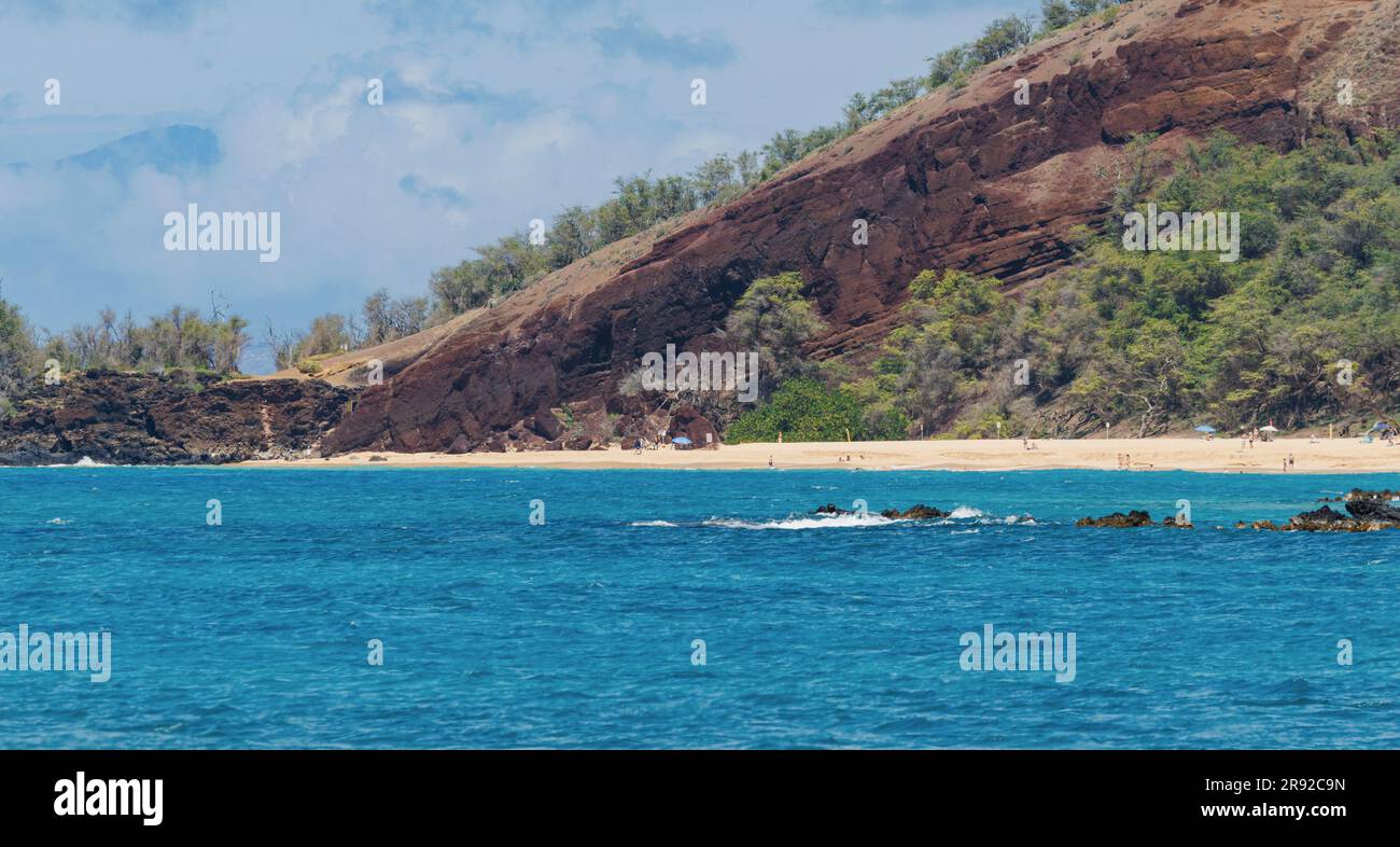 Sandstrand vor einem großen Lavafelsen mit tiefblauem Meer, wenige Urlauber baden am goldenen Sandstrand, USA, Hawaii, Maui, Kihei Stockfoto