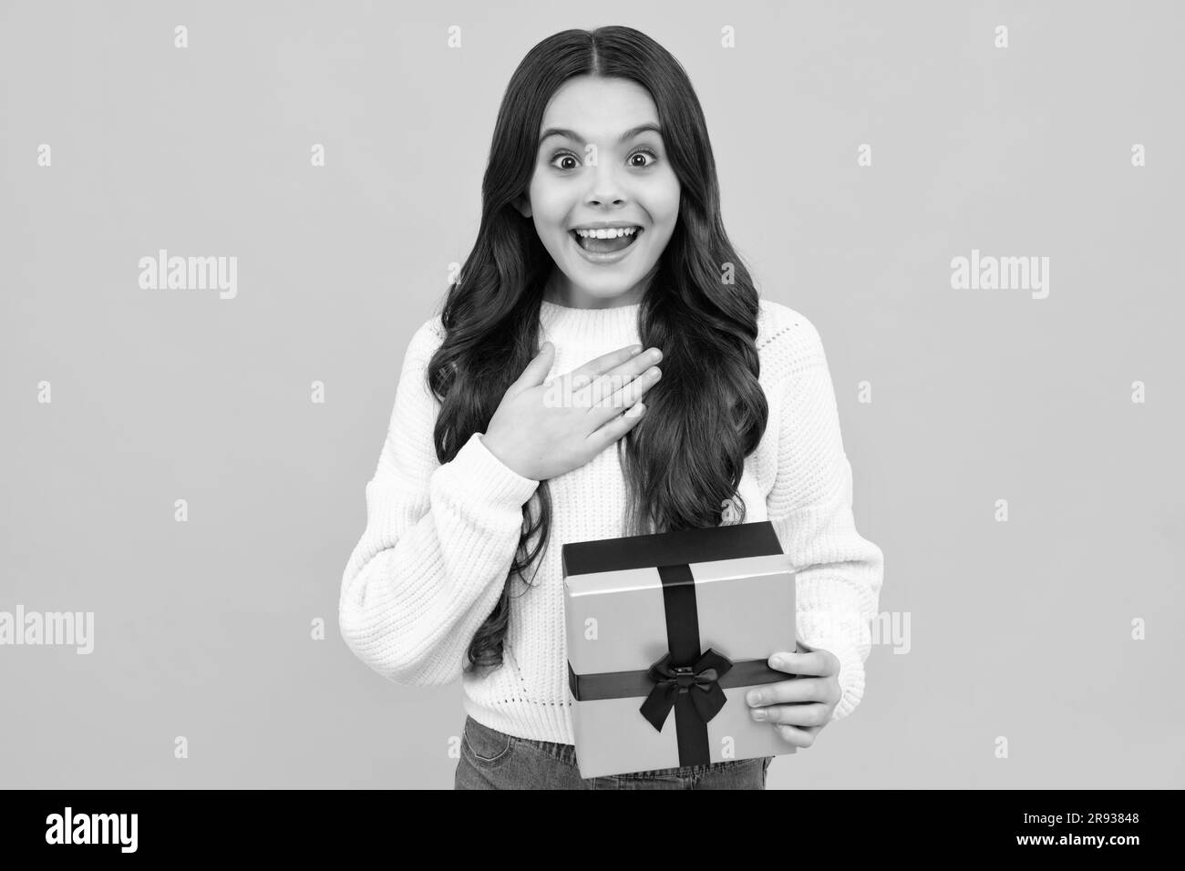 Kind mit Geschenkbox auf isoliertem gelbem Hintergrund. Geschenke zum Geburtstag, Valentinstag, Neujahr oder Weihnachten. Überraschtes Teenager-Mädchen. Stockfoto