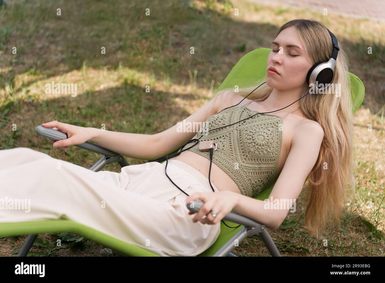 Ein Mädchen mit Kopfhörern liegt auf einer Sonnenliege und meditiert zur Musik Stockfoto