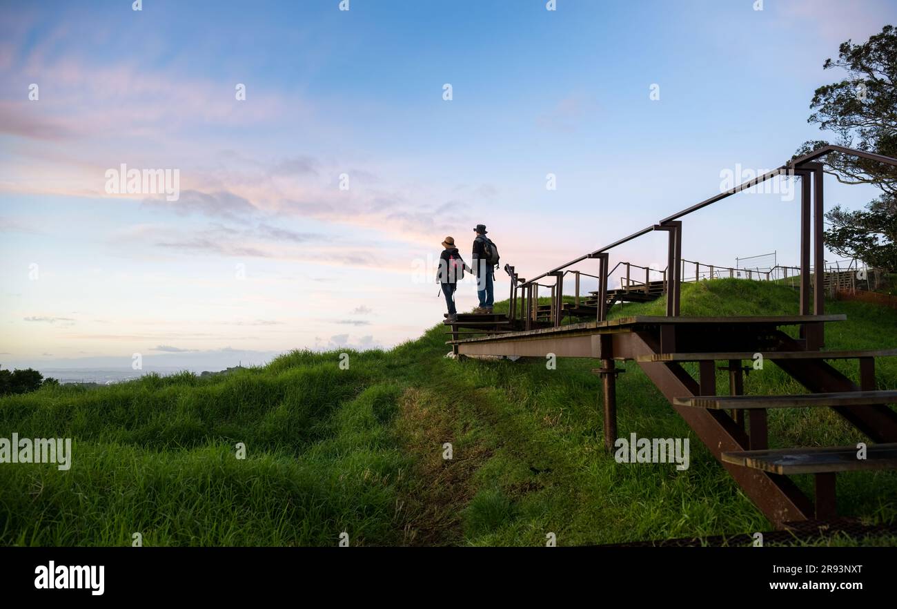 Ein Paar, das bei Sonnenaufgang auf einer erhöhten Promenade um den Krater steht. Gipfel Des Mt. Eden. Auckland. Stockfoto