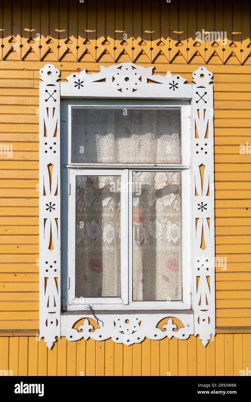 Nahaufnahme eines Fensters mit geschnitztem Holzjamb, dekoriert mit traditionellen weißen Mustern an der Fassade eines gelb gestrichenen russischen isba Stockfoto