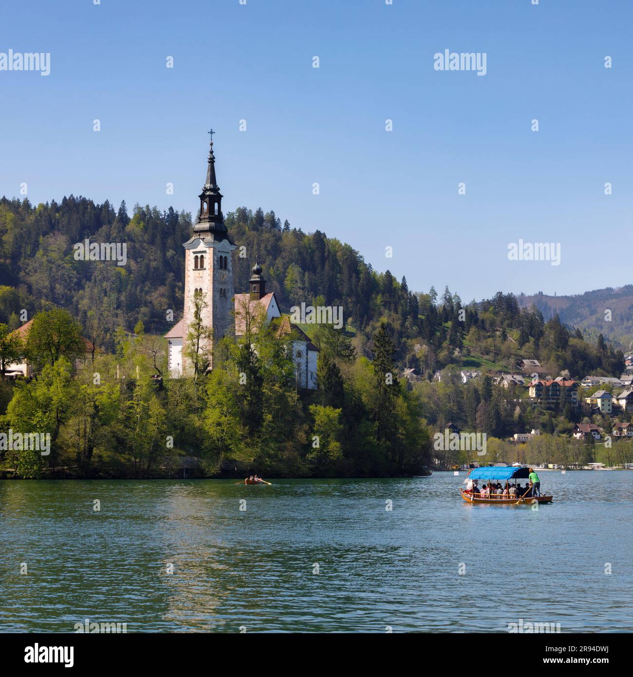 Bled, Oberkarniola, Slowenien. Kirche der Himmelfahrt auf der Insel Bled. Touristen genießen einen Bootsausflug in einem traditionellen Boot, bekannt als Pletna. Stockfoto