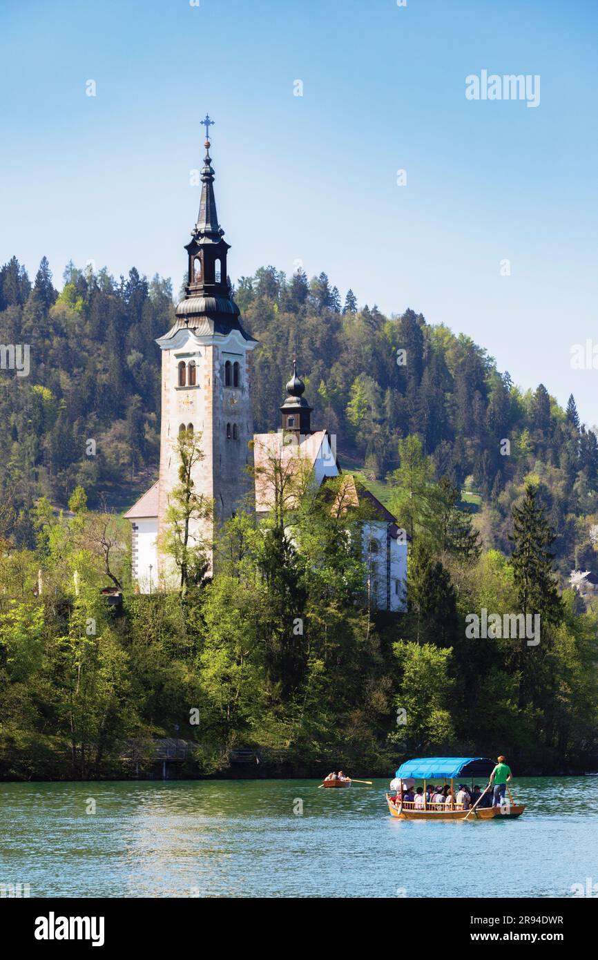 Bled, Oberkarniola, Slowenien. Kirche der Himmelfahrt auf der Insel Bled. Touristen genießen einen Bootsausflug in einem traditionellen Boot, bekannt als Pletna. Stockfoto