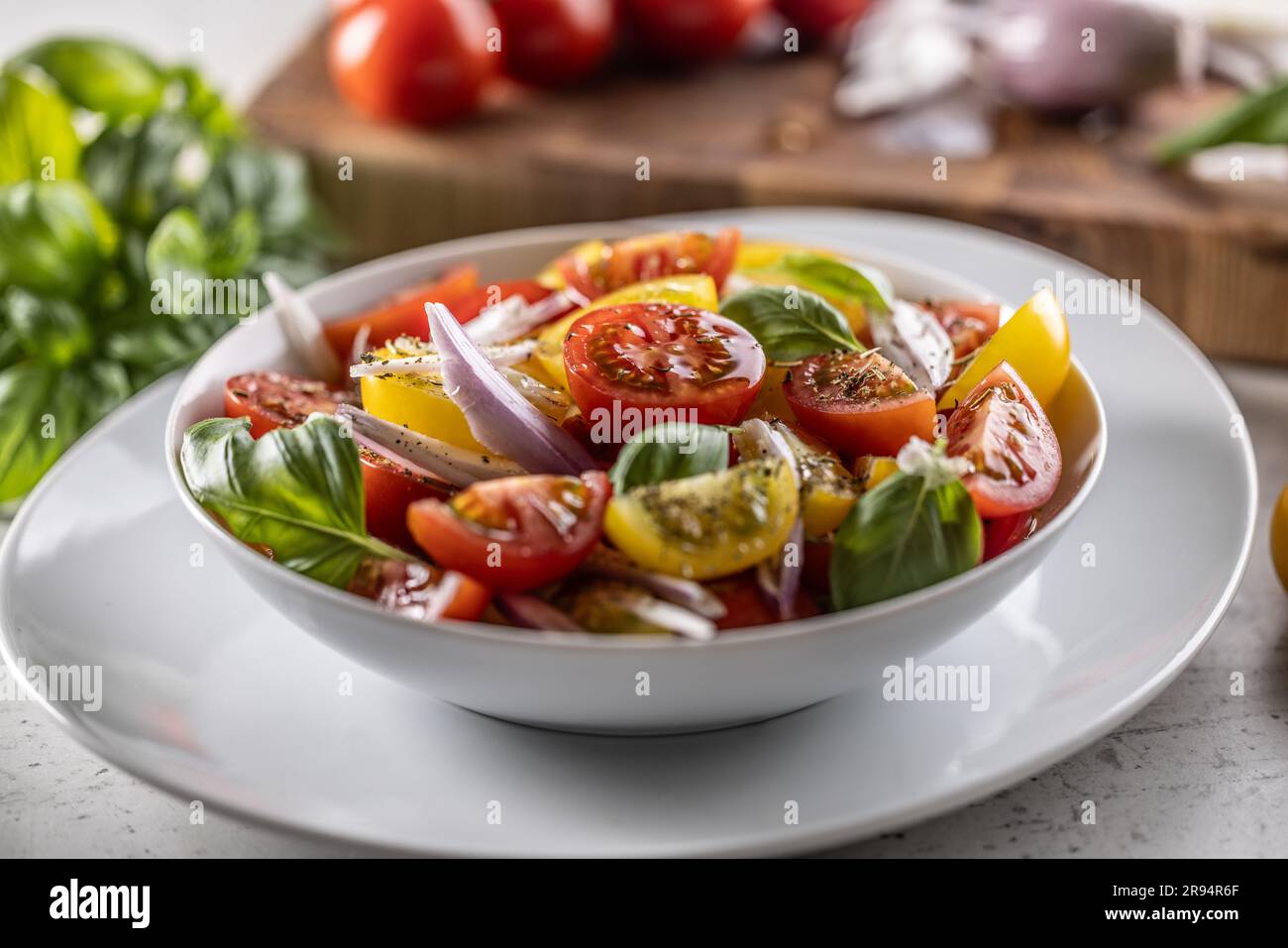 Tomatensalat mit roten Zwiebeln und Olivenöl wird in einer weißen Schüssel serviert. Stockfoto