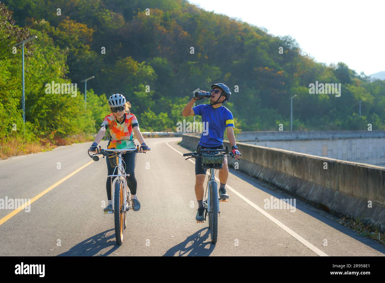 Ein müder asiatischer Radfahrer trinkt morgens Wasser aus einer Flasche, während er gemeinsam um den See reitet Stockfoto