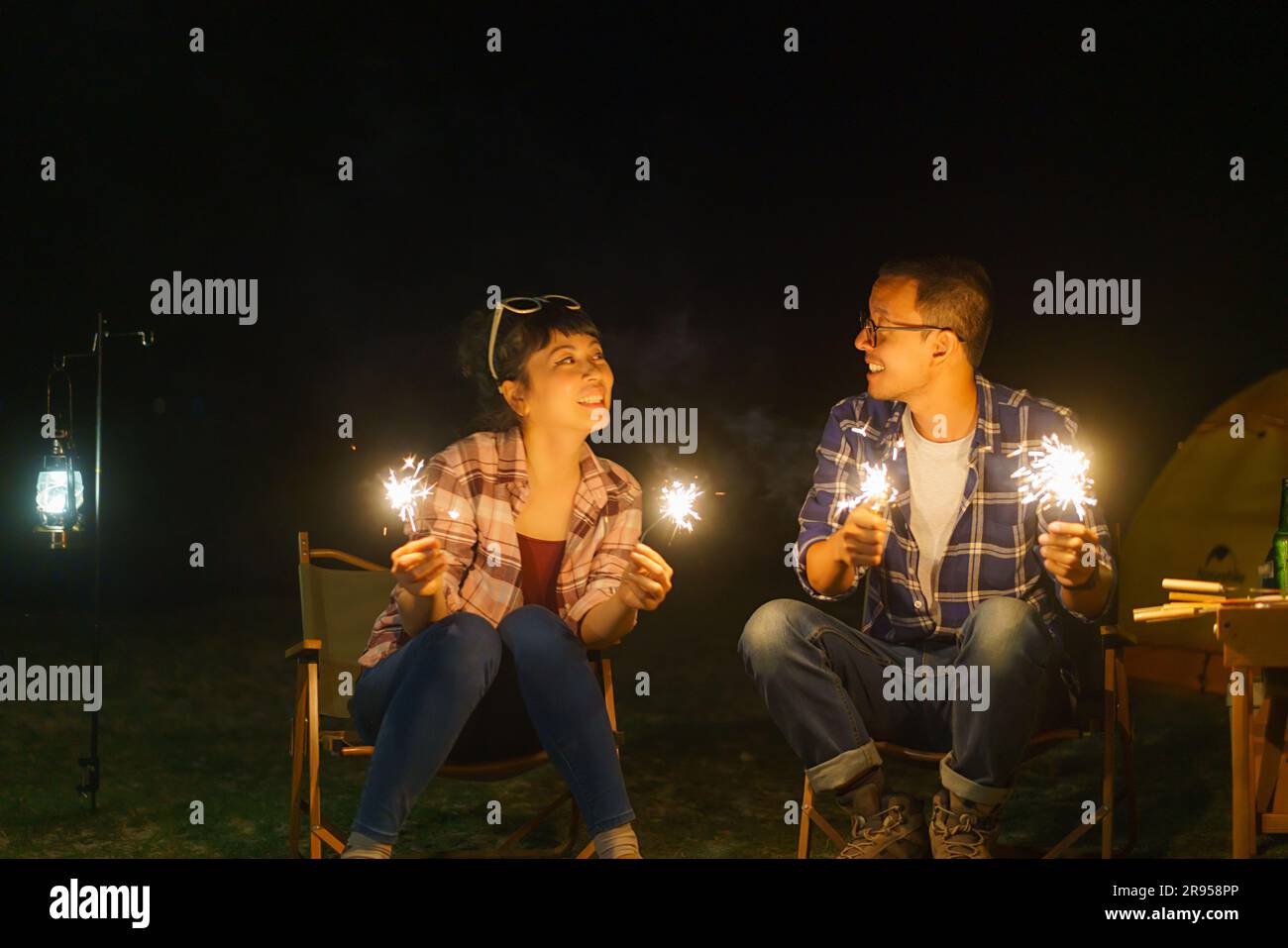 Ein asiatisches Paar zündet an einem Lagerfeuer ein funkelndes Feuer an, wo es nachts ein Zelt am See aufbaut. Stockfoto