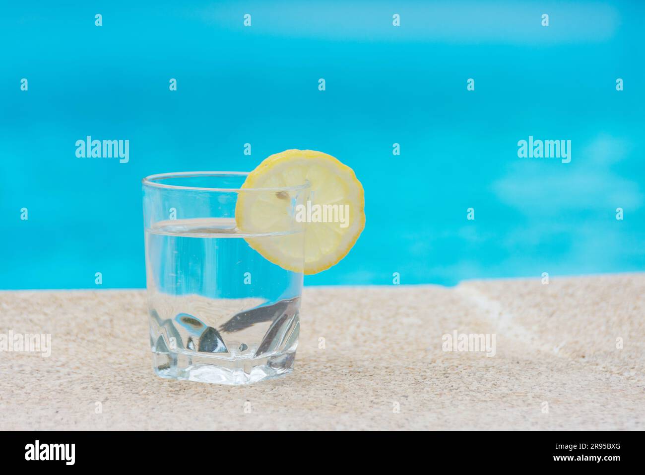 Löschen Sie Ihren Durst im Sommer, um der Hitze zu entkommen. Ein Glas Wasser mit einem Stück Zitrone am Rand eines Swimmingpools Stockfoto