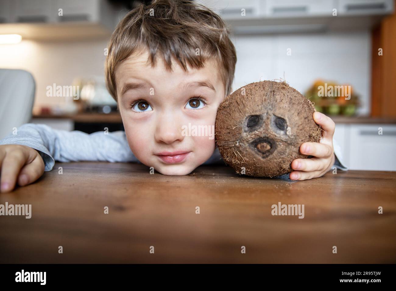 Fröhliches Porträt eines kleinen weißen Jungen mit braunen Augen am Tisch in der Küche mit einer Kokosnuss. Stockfoto