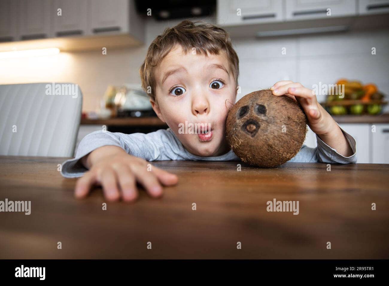 Fröhlicher, weißer Junge mit braunen Augen am Tisch in der Küche, der Spaß mit Kokosnuss hat. Stockfoto