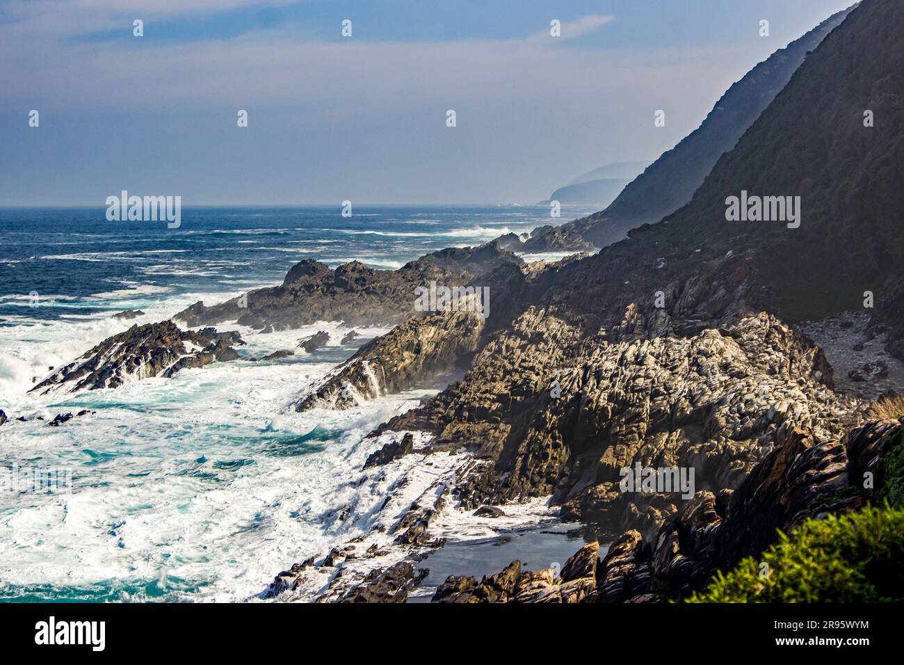 Raue Meere und Wellen brechen an der felsigen Küste und Klippen der Küste von Tsitsikamma entlang der Garden Route, Südafrika. Stockfoto