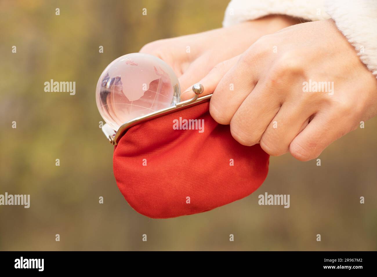 Rote leere Brieftasche mit einer transparenten Glaskugel im Blick auf den Planeten in den Händen eines Mädchens auf der Straße, weltweiter Geldmangel Stockfoto