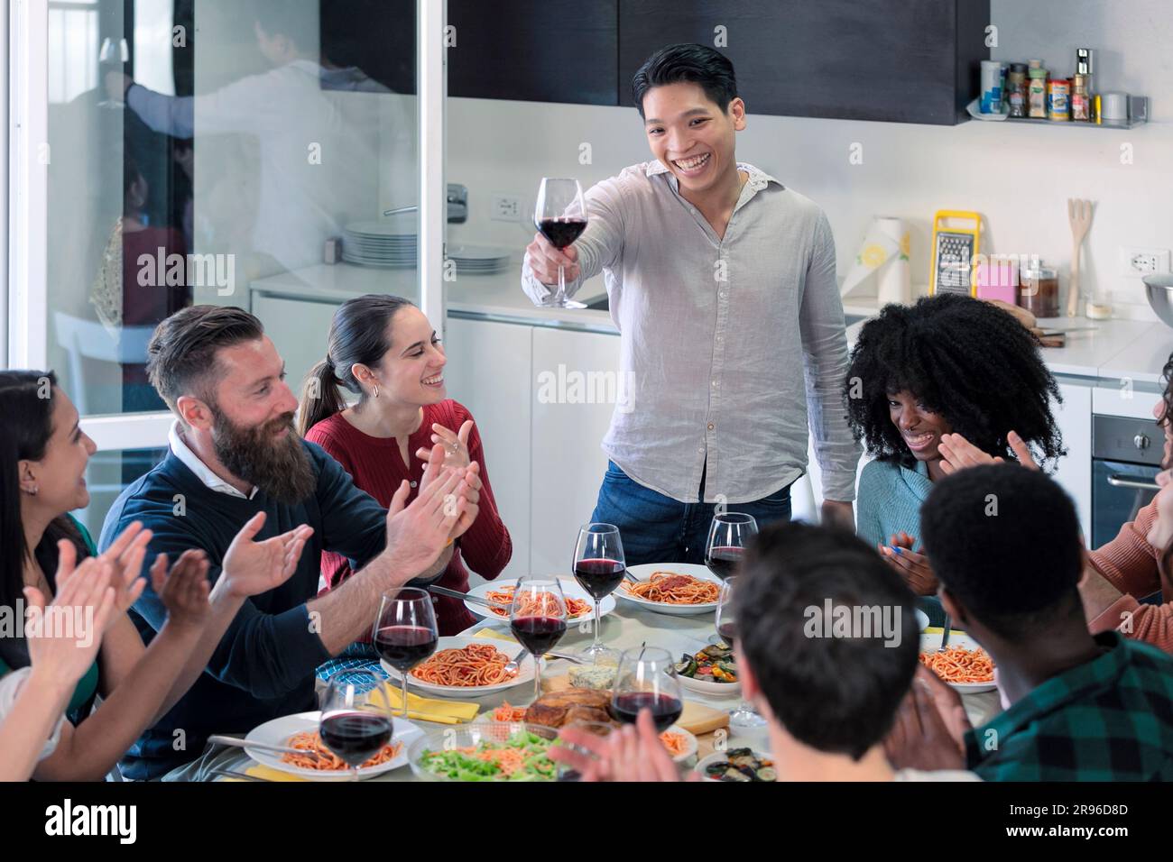Junge Freunde stoßen zusammen an, um den jungen asiatischen Mann zu feiern, Freunde trinken Wein und essen italienisches Essen Stockfoto