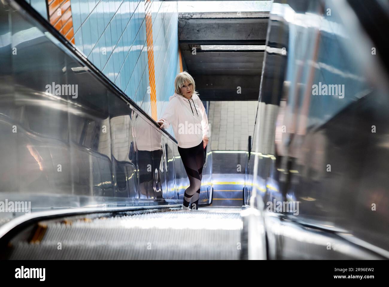 Erfundener Transvestit, Crosdresser, mit blonder Perücke und Kapuze, Porträt auf einer Rolltreppe zu einer U-Bahn-Station Köln, Nordrhein-Westfalen Stockfoto