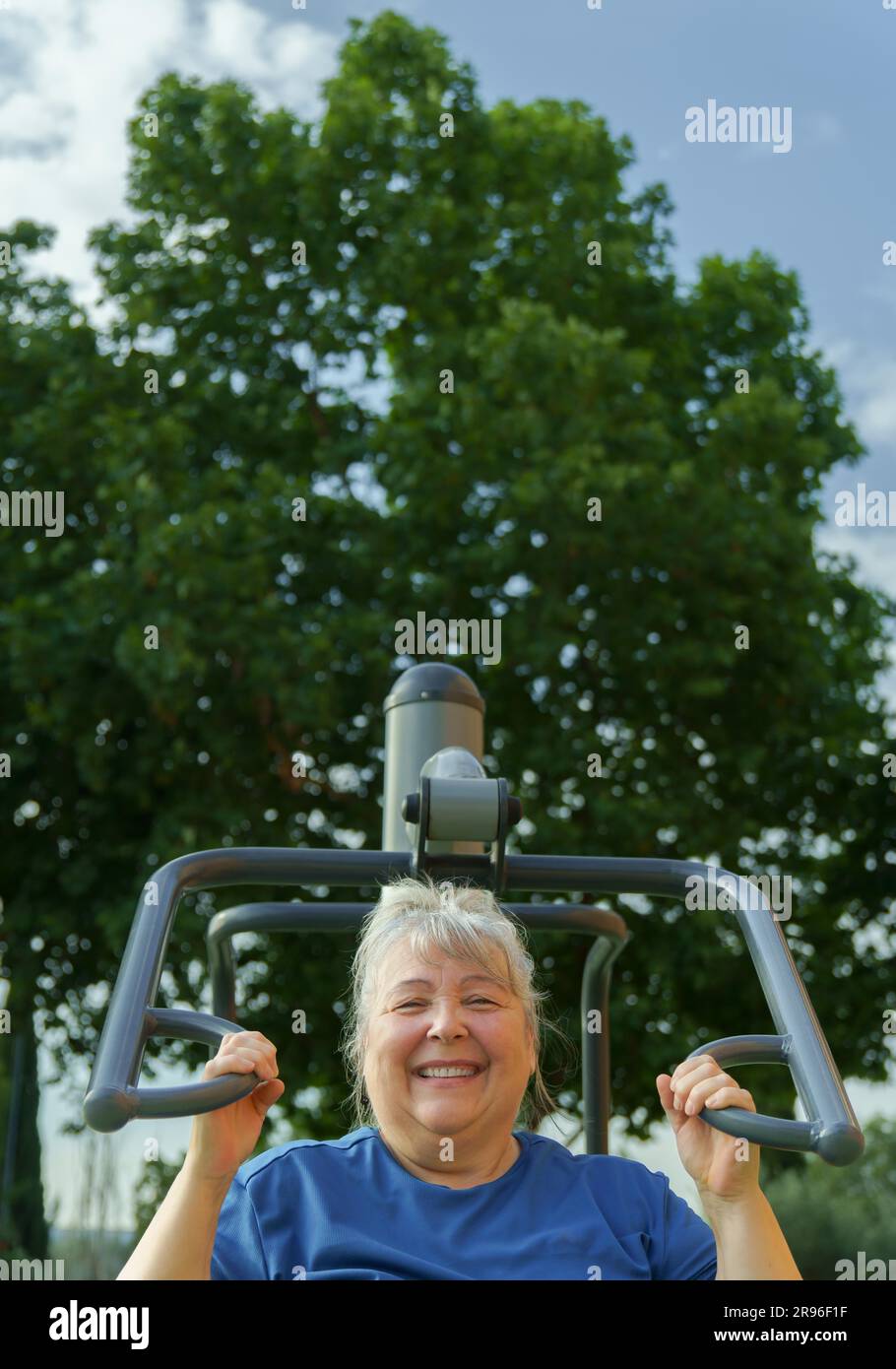Ältere fettleibige Frau in Sportbekleidung, die in einem Outdoor-Fitnessstudio in einem Park, umgeben von Bäumen, Trainingsgerät, gesundem Lebensstil und schlankem Design trainiert Stockfoto