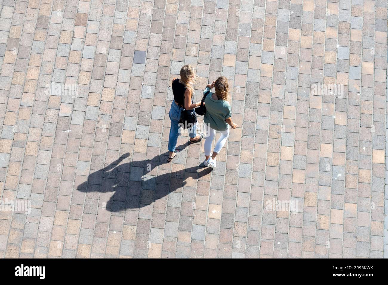 Zwei Frauen, die auf einem öffentlichen Platz spazieren und lange Schatten werfen, von einem hohen Gebäude aus gesehen. Stockfoto