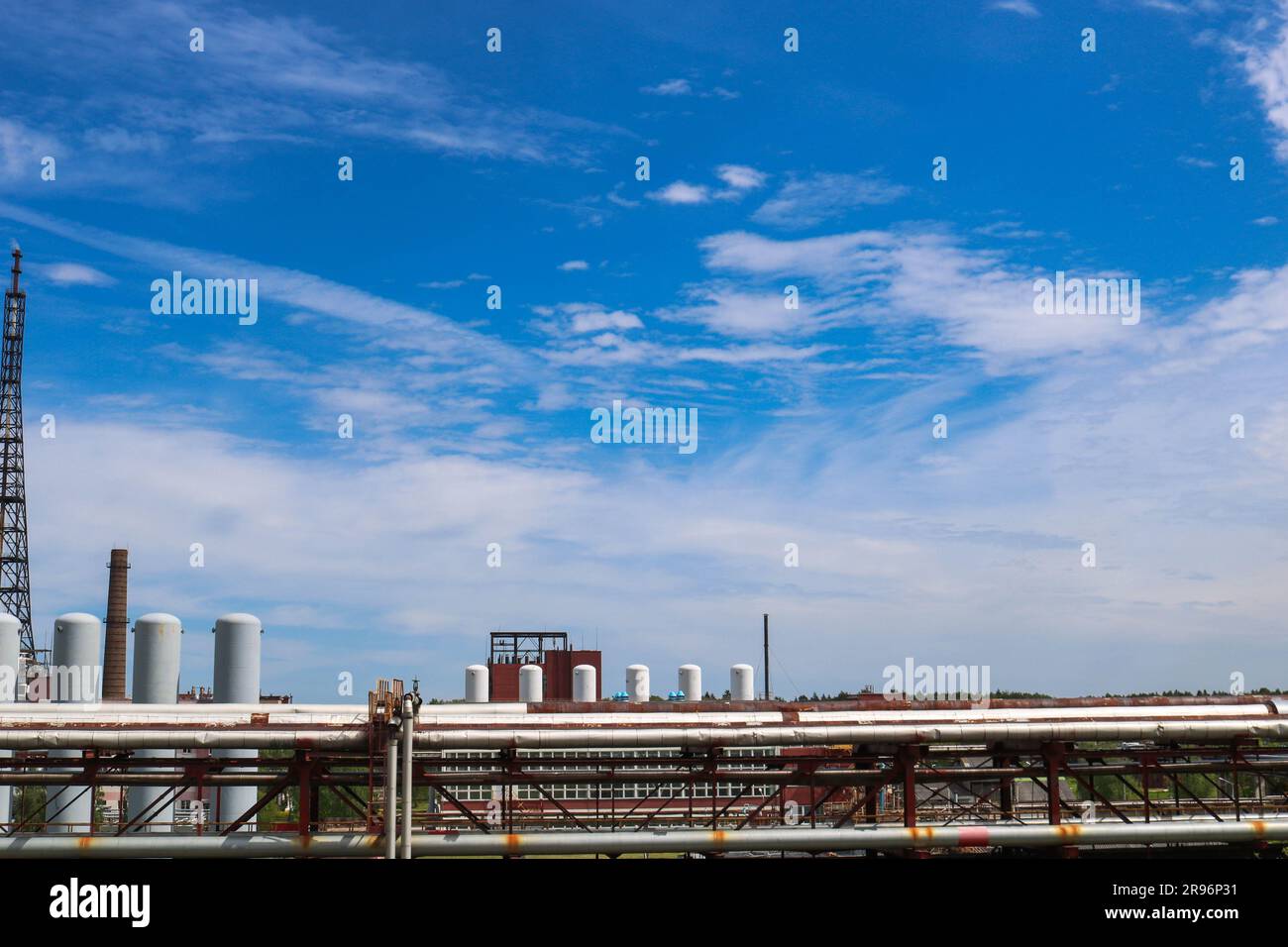 Blick auf eine Rohrleitungsüberführung mit Rohren, Tanksäulen vor blauem Himmel mit Wolken in einer petrochemischen Raffinerie. Stockfoto