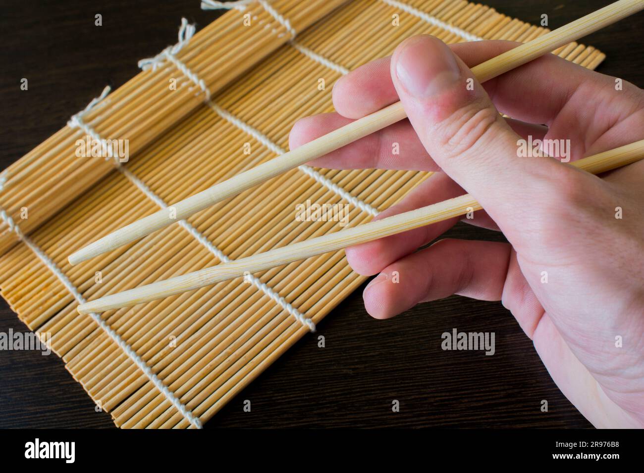 Stäbchen in der Hand auf dem Hintergrund einer Sushi-Matte Stockfoto