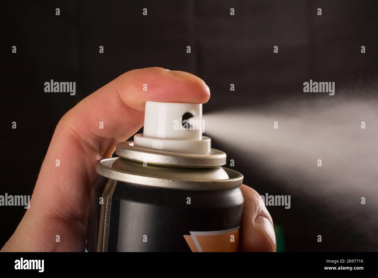 Nahaufnahme einer menschlichen Hand und einer gepressten Sprühflasche auf schwarzem Hintergrund Stockfoto