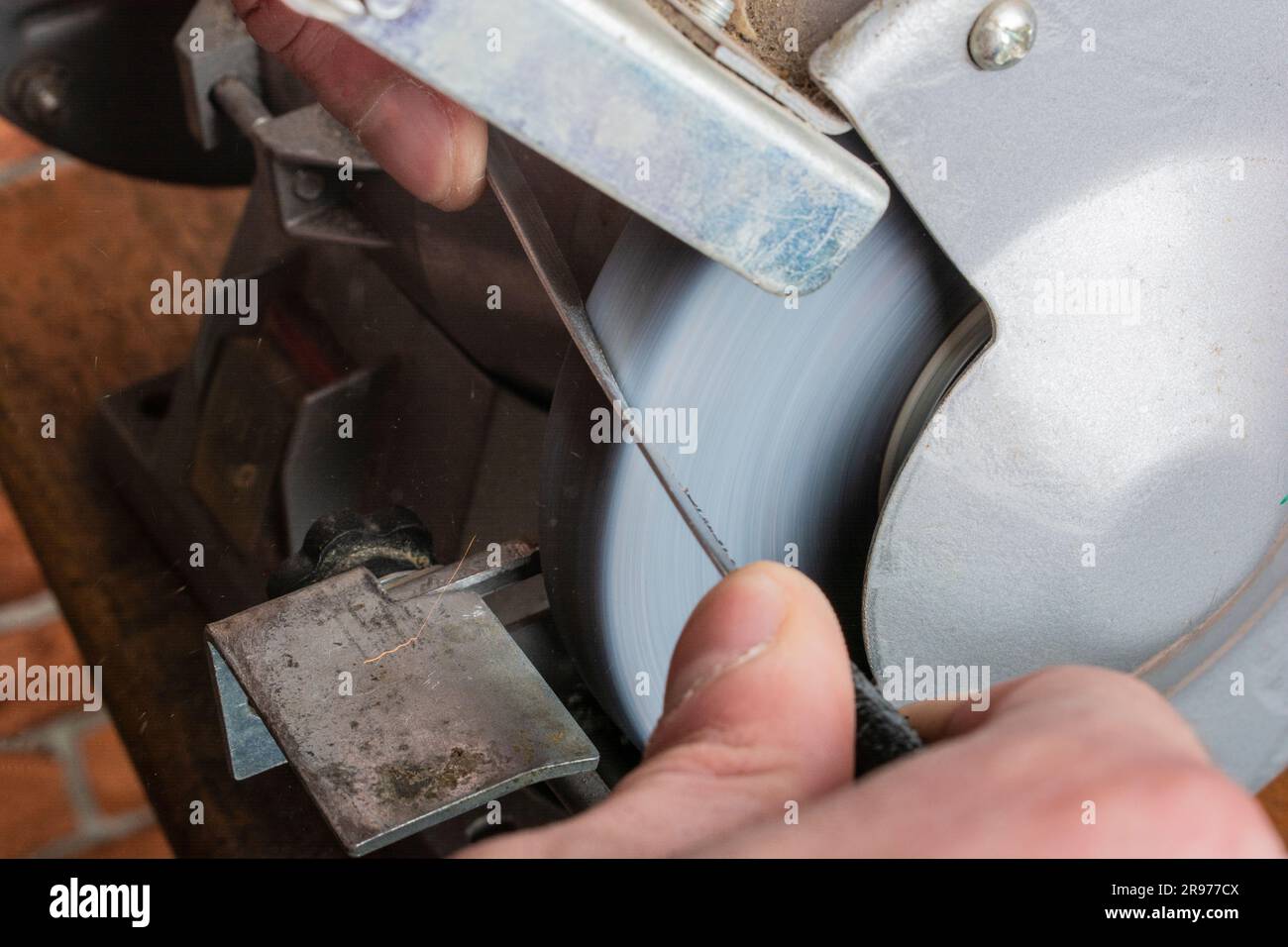 Ein Messerschärfer und eine Hand mit Klinge auf einem Holztisch, Nahaufnahme vor einem Backsteinhintergrund Stockfoto