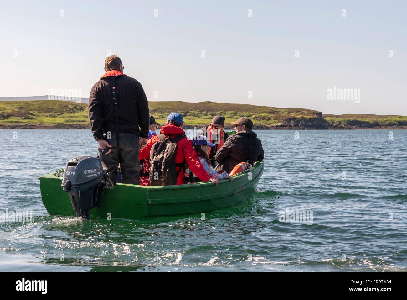 Dunvegan, Isle of Skye, Schottland, Großbritannien. Touristen mit Rucksäcken reisen in einem kleinen grünen Boot mit Außenbordmotor über Loch Dunvegan im westen Stockfoto