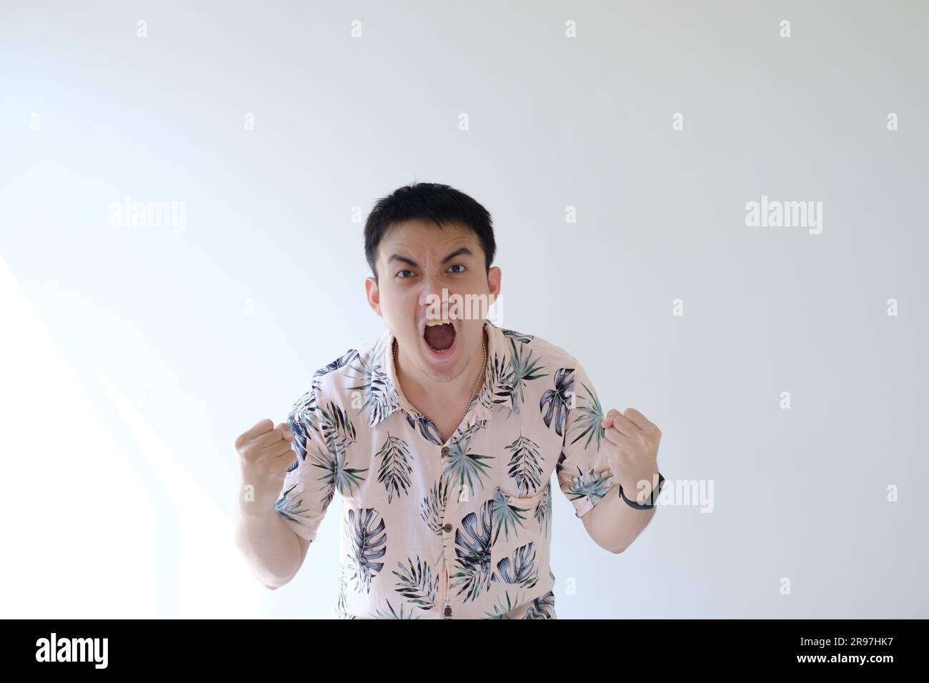 Ein junger asiatischer Mann, der ein rosafarbenes Hemd mit tropischen Mustern und einer Smartwatch am linken Handgelenk trägt, ist glücklich und aufgeregt und zeigt seinen Ausdruck Stockfoto