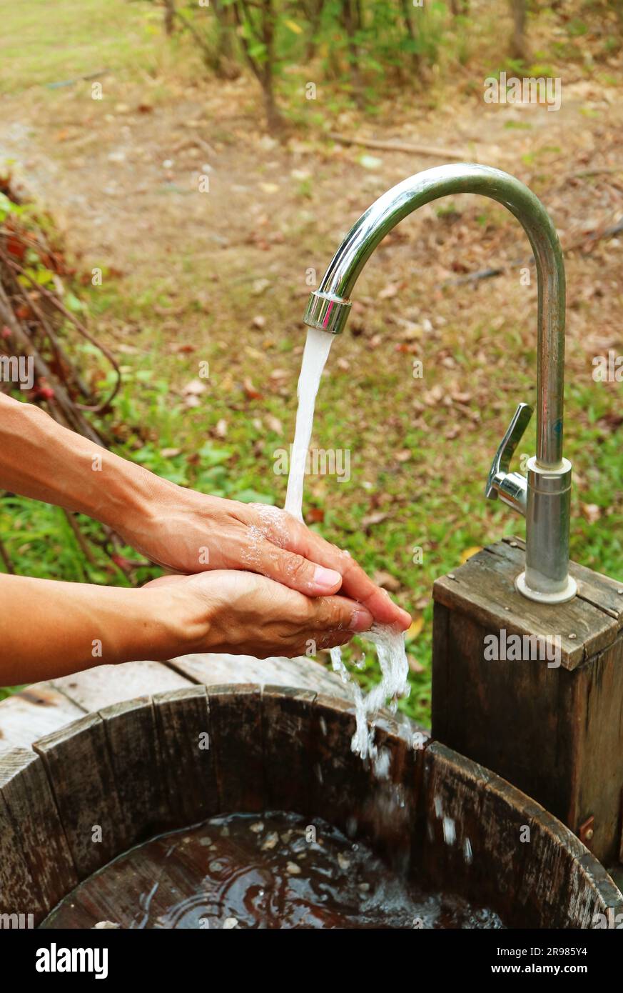 Die Hände des Mannes unter dem fließenden Wasser vom Wasserhahn im Garten Stockfoto