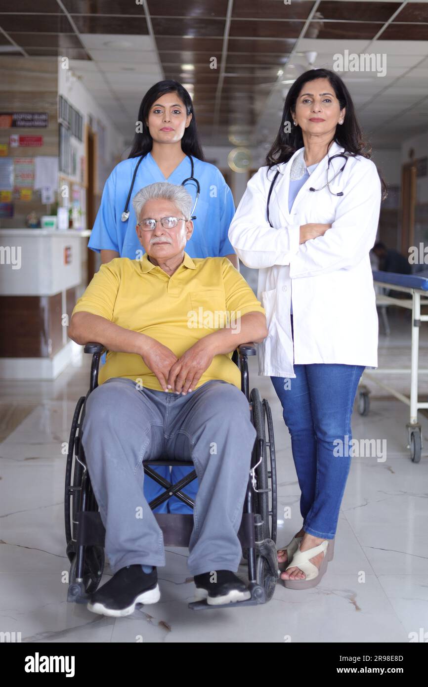 Indische Krankenschwester sieht sehr glücklich aus, grüßt einen älteren Patienten im Rollstuhl im Krankenhaus und lächelt - Healthcare-Konzepte. Stockfoto